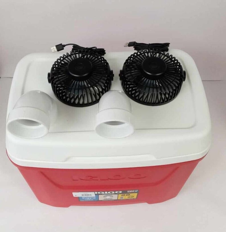 May include: A red Igloo cooler with two black USB-powered fans attached to the top. The fans have white plastic housings and are connected to the cooler with white PVC pipes.