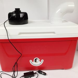 May include: A red cooler with a white lid and a black fan on top. The cooler has a white sticker with a penguin logo and the text "coolercampcooler.com". A white plastic pipe is attached to the lid. A black power cord connects the fan to a black power adapter.