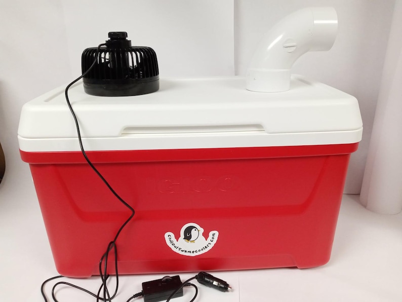 May include: A red cooler with a white lid and a black fan on top. The cooler has a white sticker with a penguin logo and the text "coolercampcooler.com". A white plastic pipe is attached to the lid. A black power cord connects the fan to a black power adapter.