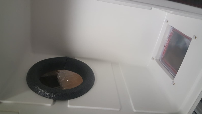 May include: A white interior with a black foam ring and a rectangular opening with a red frame.
