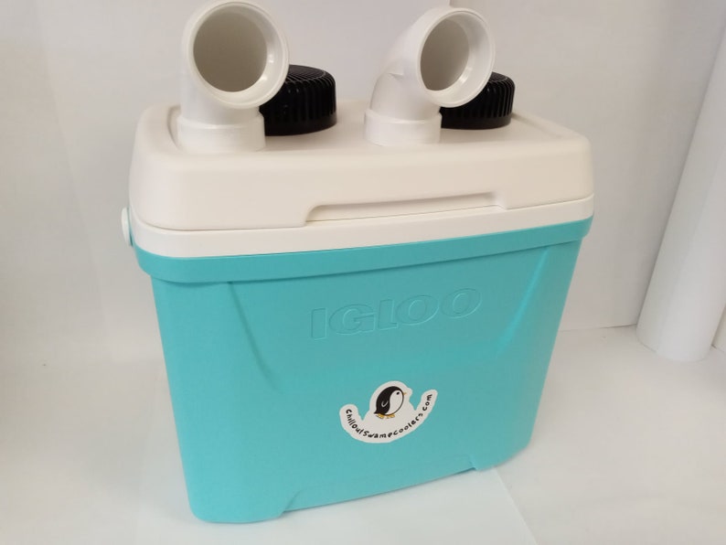 Pode incluir: Uma caixa t&eacute;rmica Igloo turquesa com duas bicas de pl&aacute;stico branco no topo. A caixa t&eacute;rmica tem um logotipo de pinguim preto e branco com o texto "igloocoolers.com".