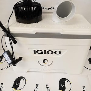 May include: A white Igloo cooler with a black fan, white duct, and power adapter. The cooler has a gray top and the text "IGLOO" in black. The logo "Chillout Swampcoolers.com" is also visible.