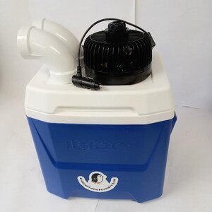 Peut inclure: Glaci&egrave;re Igloo bleue et blanche avec un ventilateur noir et des conduits d'air blancs. L'autocollant sur la glaci&egrave;re indique "Chillout Swampcoolers.com". Le ventilateur a un cordon noir avec un adaptateur de voiture.