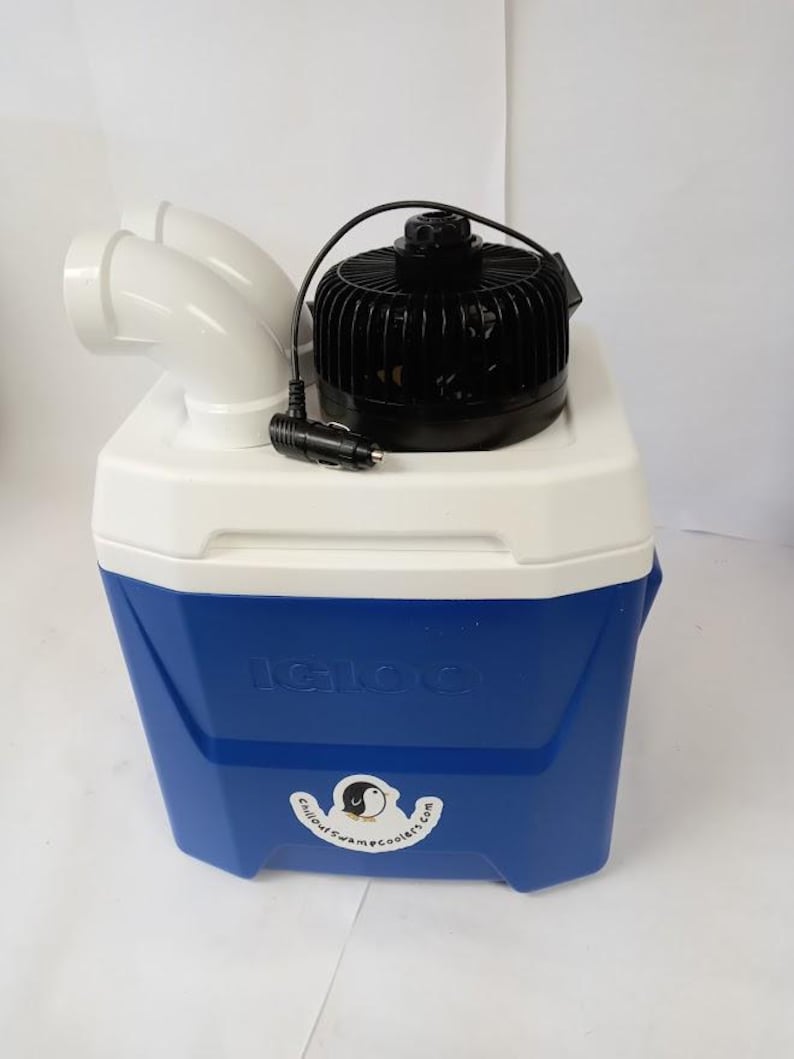 Peut inclure: Glaci&egrave;re Igloo bleue et blanche avec un ventilateur noir et des conduits d'air blancs. L'autocollant sur la glaci&egrave;re indique "Chillout Swampcoolers.com". Le ventilateur a un cordon noir avec un adaptateur de voiture.