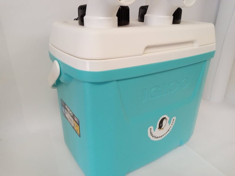 Pode incluir: Uma caixa t&eacute;rmica turquesa com uma tampa branca e um adesivo de pinguim que diz "chilledswampenguins.com". A caixa t&eacute;rmica tem uma al&ccedil;a e um logotipo "IGLOO" no lado.