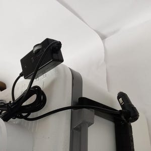 Puede incluir: Un adaptador de corriente negro con una perilla y un cable conectado a una nevera blanca con un asa negra.