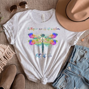 Puede incluir: Una camiseta blanca con un gr&aacute;fico de lib&eacute;lula colorido y el texto "Whisper words of wisdom, let it be".