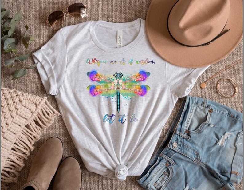 Puede incluir: Una camiseta blanca con un gr&aacute;fico de lib&eacute;lula colorido y el texto "Whisper words of wisdom, let it be".