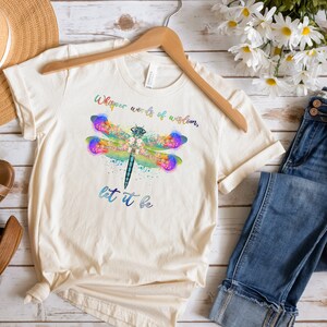 Puede incluir: Una camiseta de color crema con un dise&ntilde;o de lib&eacute;lula acuarela y el texto "Whisper words of wisdom, let it be".