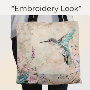 May include: Tote bag with a hummingbird design. The bag features a detailed embroidered hummingbird with turquoise wings, a long black beak, and a green head. Pink, blue, and purple flowers are at the bottom left. The text "*Embroidery Look*" is at the top.