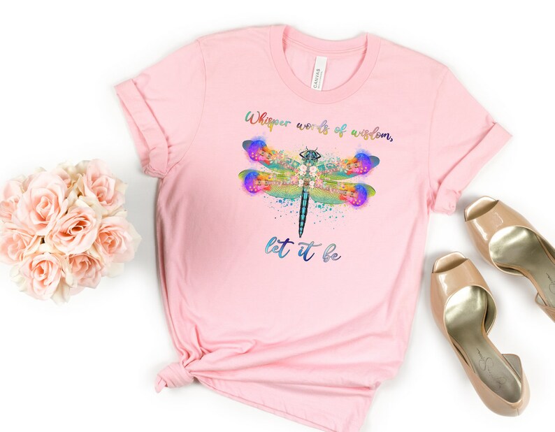 Puede incluir: Camiseta rosa con un dise&ntilde;o de lib&eacute;lula acuarela y el texto "Whisper words of wisdom, let it be".