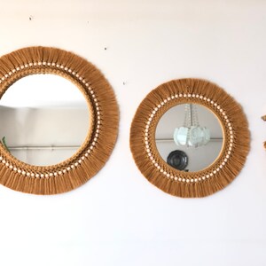 May include: Two round mirrors with a brown macrame frame and white beads around the edge. A smaller brown macrame feather wall hanging with white beads.