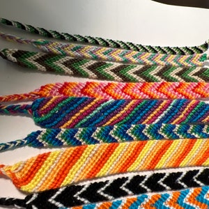 May include: A collection of colorful friendship bracelets with chevron patterns. The bracelets are made with different colored threads and are woven together in a zig-zag pattern.