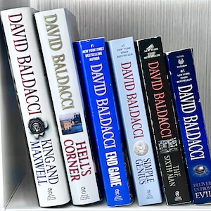 May include: A collection of hardcover books by David Baldacci, including "King and Maxwell," "Hell's Corner," and "End Game." The spines display titles in white and red lettering against various colored backgrounds, with the author's name prominently featured.
