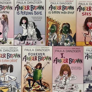 May include: A collection of children's books by Paula Danziger, featuring the title character Amber Brown. The book covers are in various colors, with illustrations of Amber Brown and related scenes. The titles include "Amber Brown is Feeling Blue" and "Forever Amber Brown."