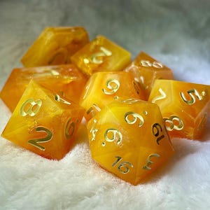 May include: A set of eight yellow and gold dice with white numbers. The dice are made of a translucent material and have a speckled appearance.