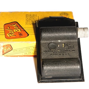 May include: Vintage Rol-Bak 16mm film camera with its original yellow and orange box. The camera is black with a silver winding knob. The box has the Rol-Bak logo and text. Made in the U.S.A.