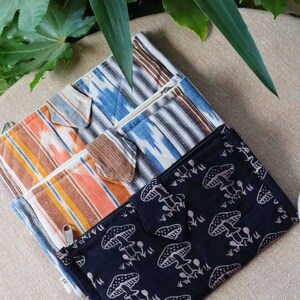 Op de afbeelding: Een verzameling kleurrijke stoffen portemonnees. De portemonnees hebben verschillende patronen, waaronder strepen en een paddenstoelprint. De portemonnees hebben ritssluitingen en een klepsluiting. De kleuren zijn blauw, oranje, bruin en zwart.