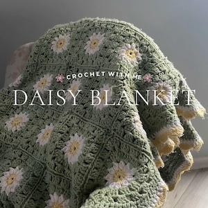 Op de afbeelding: Een gehaakt groen en wit deken met daisy-motief en een gele rand. Het deken is over een houten stoel gelegd. De tekst "CROCHET WITH ME" en "DAISY BLANKET" is zichtbaar in de afbeelding.