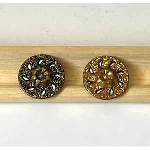 May include: Two ornate gold-toned buttons with a raised, star-shaped center and a decorative, swirling pattern around the edge.