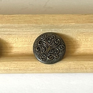 May include: A round, ornate, bronze-colored button with a floral design.