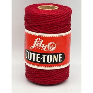 May include: A spool of red Lily Jute-Tone twine. The label is red with white and black text. The spool is cylindrical and made of tightly wound jute fibers. The product is for crafts and DIY projects.