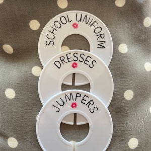 May include: Three white plastic hanger labels with a small pink flower design. The labels are labelled "School Uniform", "Dresses", and "Jumpers".