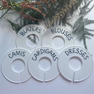 May include: Five white plastic hanger labels with black text. The labels are for organising clothes and are labelled "Blazers", "Blouses", "Camis", "Cardigans", and "Dresses".