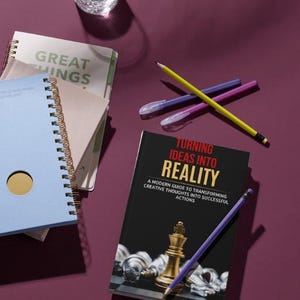 May include: A still life arrangement featuring a glass of water, notebooks, pens, and a book titled "TURNING IDEAS INTO REALITY." The book cover is black with gold and white accents. Pencils and pens are scattered around the book and notebooks.