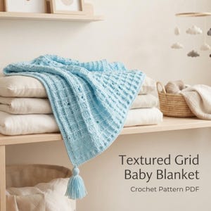 May include: A light blue crochet baby blanket featuring a textured grid pattern and a single tassel at the corner. The text "Textured Grid Baby Blanket Crochet Pattern PDF" is visible on the right side of the image near the folded blanket.