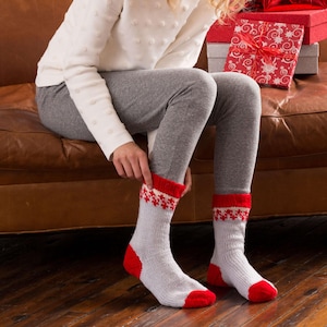 May include: A pair of mid-calf knit socks featuring a light gray base with vibrant red heels, toes, and cuffs. The cuffs are accented with a white and red snowflake-inspired geometric pattern, providing a festive look for the winter season.