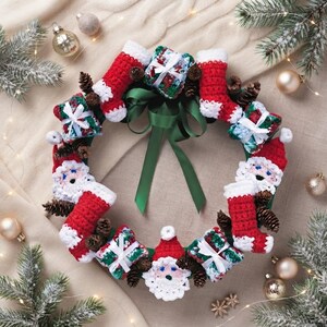 Puede incluir: Una corona navideña con figuras de Papá Noel tejidas a ganchillo, calcetines rojos y blancos y pequeños regalos con lazos blancos. La corona está decorada con piñas marrones y un lazo central de satén verde oscuro para colgarla.