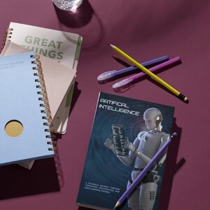 K&ouml;nnte beinhalten: Ein Stillleben mit einem Glas Wasser, Notizb&uuml;chern, Stiften und Bleistiften auf einer weinroten Oberfl&auml;che. Das Buch mit dem Titel "Artificial Intelligence" ist sichtbar, zusammen mit anderen Notizb&uuml;chern mit dem Text "Great Things".
