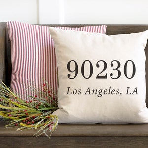 May include: A white throw pillow with the text "90230 Los Angeles, LA" printed in black.
