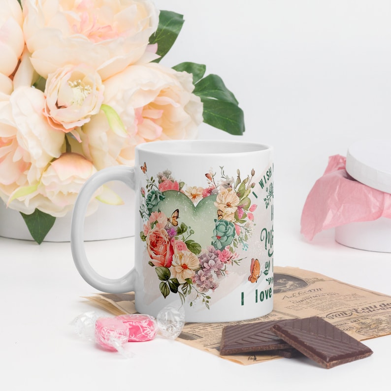 May include: White ceramic mug with a floral design and a green heart. The text on the mug reads "I wish you a day filled with love and happiness.  I love you, Mom".