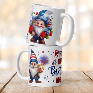Op de afbeelding: Twee witte keramische mokken met een patriottisch thema. De bovenste mok heeft een gnome die een rood, wit en blauwe hoed draagt en een boeket bloemen vasthoudt. De onderste mok heeft een gnome die een rood, wit en blauwe hoed draagt en een boeket bloemen en vuurwerk vasthoudt. De tekst op de onderste mok is "Happy Birthday America".