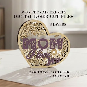 Puede incluir: Decoración de madera en forma de corazón con recortes florales y la palabra "MOM" en morado. La frase "I love you" también es visible. El texto "DIGITAL LASER CUT FILES" está en la parte superior. El diseño tiene 8 capas.