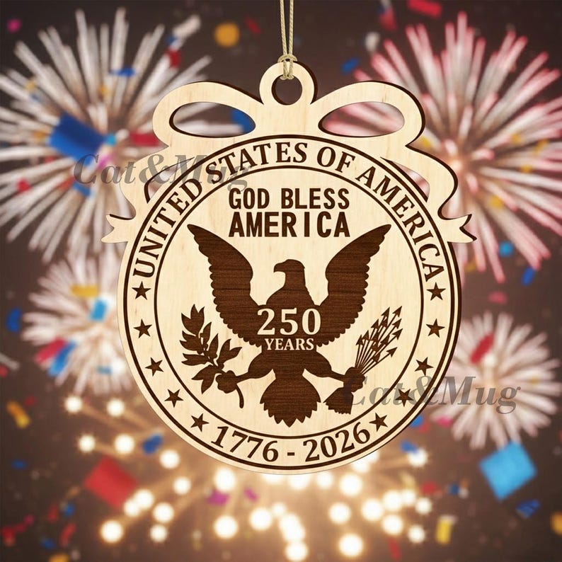 Peut inclure: Ornement en bois avec l'inscription "United States of America" et "God Bless America". Il pr&eacute;sente un aigle, le texte "250 Years" et les dates "1776-2026". L'ornement est con&ccedil;u avec un n&oelig;ud en haut pour &ecirc;tre suspendu.