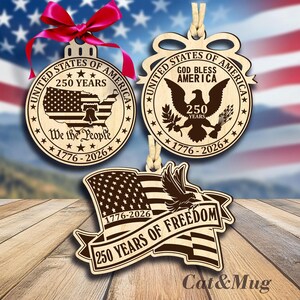 Peut inclure: Trois d&eacute;corations de No&euml;l en bois sur le th&egrave;me patriotique. L'une est ronde avec une carte des &Eacute;tats-Unis et le texte "250 Years" et "We the People". Une autre pr&eacute;sente un aigle et le texte "God Bless America". La troisi&egrave;me est un drapeau avec un aigle et le texte "250 Years of Freedom".