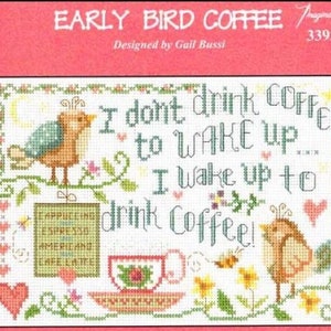 May include: Cross stitch pattern featuring a bird with the text "I don't drink coffee to wake up, I wake up to drink coffee!" and a cup of coffee. The pattern also includes a variety of flowers and leaves.