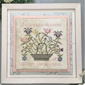 May include: A framed cross stitch sampler with a floral design and the text "All most have flowers... always and always..." The frame is white with a light blue and pink mat.