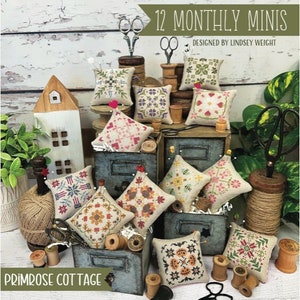May include: A collection of small, square, embroidered pillows with various floral and geometric designs. The pillows are arranged on and around vintage-style wooden boxes, with spools of thread, scissors, and the text "12 MONTHLY MINIS" and "PRIMROSE COTTAGE".