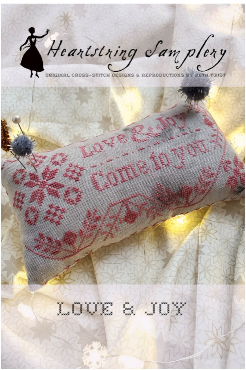 May include: A white and pink cross-stitch sampler with the text "Love & Joy - Come to you" and the words "Love & Joy" at the bottom. The sampler is on a white fabric with a snowflake pattern.