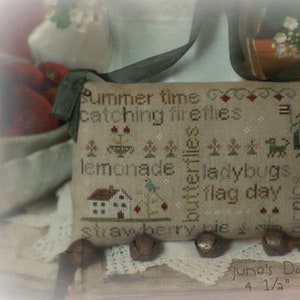 May include: A beige cross-stitch pillow with summer-themed words and images, including a house, dog, and bottle. The text includes "Summer time", "catching fireflies", and "June". The pillow measures 4 1/2" x 7 1/2".