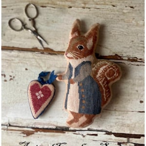 May include: Cross stitch pattern featuring a cute squirrel holding a red heart. The pattern is part of the Animal Crackers Series and is titled "Miss Hazel".