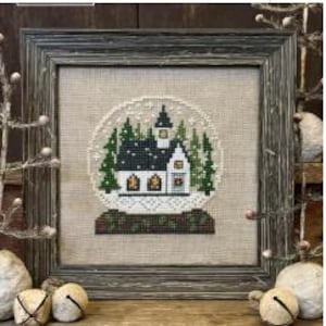 May include: Framed cross-stitch art featuring a snow globe design with a church, pine trees, and falling snow. The artwork is set against a neutral background and framed in a rustic, gray wooden frame. The overall theme is winter and Christmas.