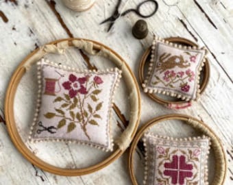 May include: Three embroidery hoops with different designs. The first hoop has a floral design with pink flowers and green leaves. The second hoop has a design of a rabbit with pink flowers and green leaves. The third hoop has a geometric design with a pink and white pattern.