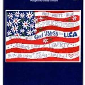 May include: A cross-stitch pattern featuring a stylized American flag design. The flag incorporates red and white stripes, with a field of white daisies and text that reads "RED, WHITE & BLOOM", "FREEDOM", "GOD BLESS THE USA", "SWEET LAND OF LIBERTY", and "HAPPY BIRTHDAY USA".