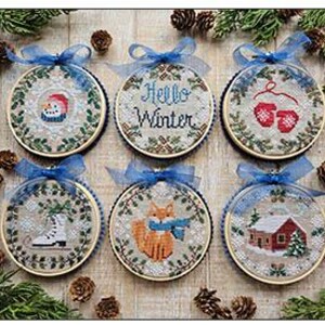 May include: Six embroidered winter-themed ornaments. Each circular ornament features a different design: a snowman, the text "Hello Winter", mittens, ice skates, a fox, and a house. Each ornament is framed in a wooden hoop and has a blue ribbon for hanging.
