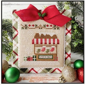 May include: A cross-stitch design featuring a Christmas stocking shop with red and white striped awning and the word "STOCKINGS". The design is framed with a red bow and plaid fabric.